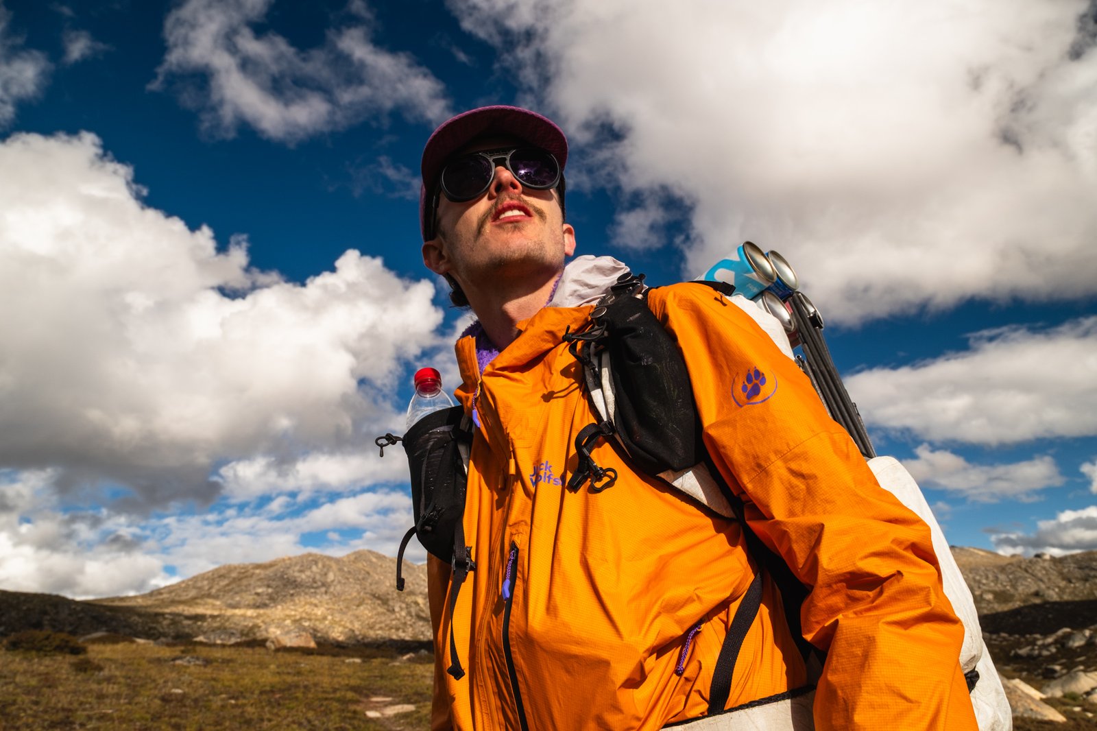 Timothy wearing an orange shell and carrying a hiking pack beneath a blue sky