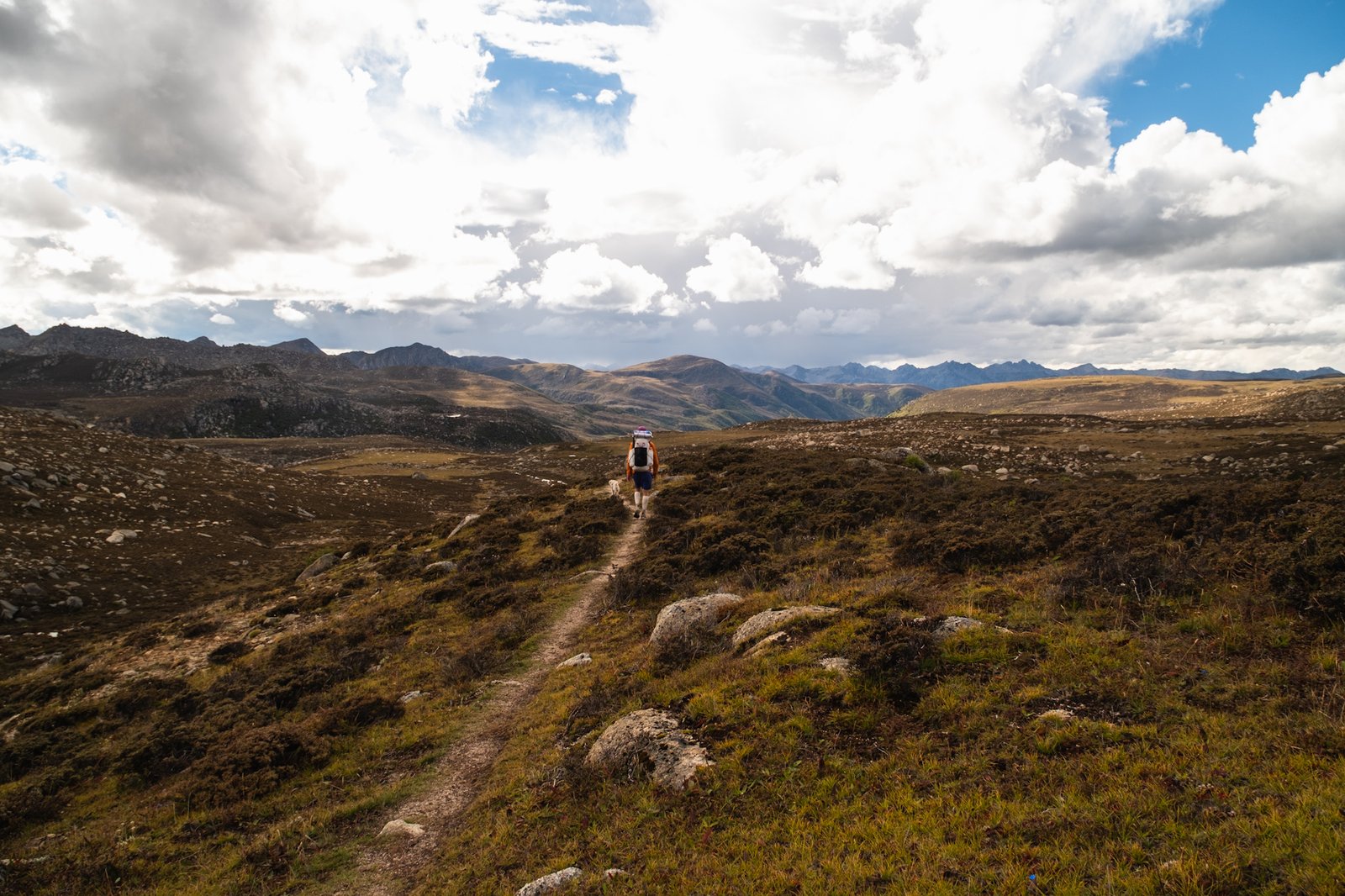 A lone hiker walking a narrow trail across open mountain terrain